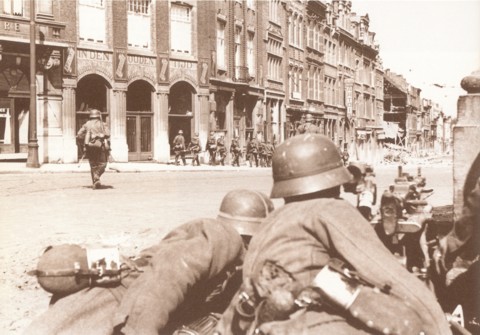 Het Stationsplein tijdens de oorlog. Het gebouw langs waar de soldaten passeren (met het halfrond balkon met gietijzeren leuning) is de 'Brasserie Nationale'. Het zou enkele jaren later het clublokaal van de Dijlezwaluw worden.